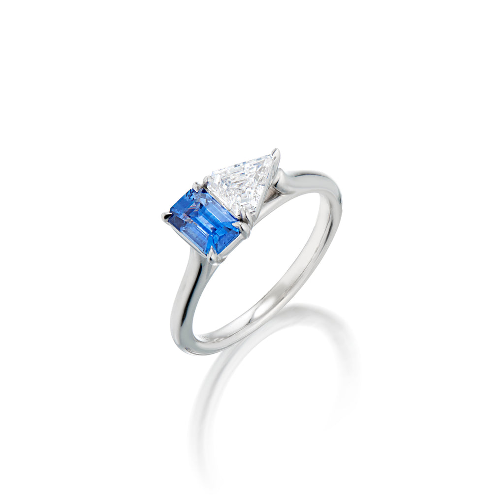 White gold ring with emerald-cut blue sapphire gemstone flanked up against a kite -shaped diamond upright on an angle