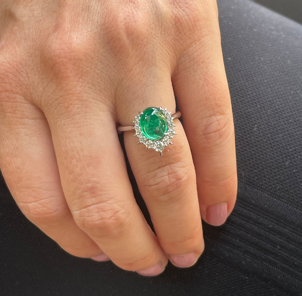 Centred oval-Shaped emerald surrounded by sparkling diamonds, set in a white gold band on finger