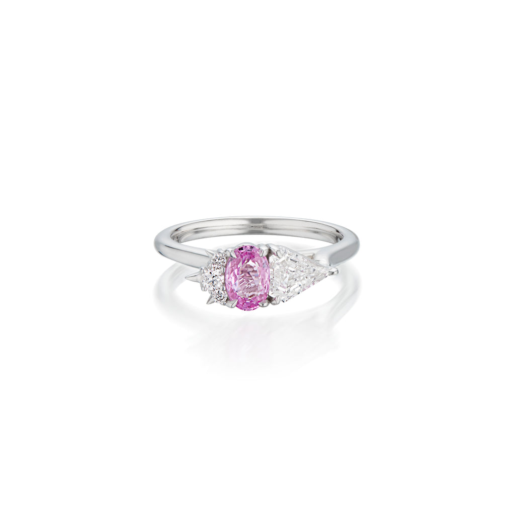 White gold ring with a centred pink oval sapphire gemstone flanked by  triangular and round diamonds on white background.