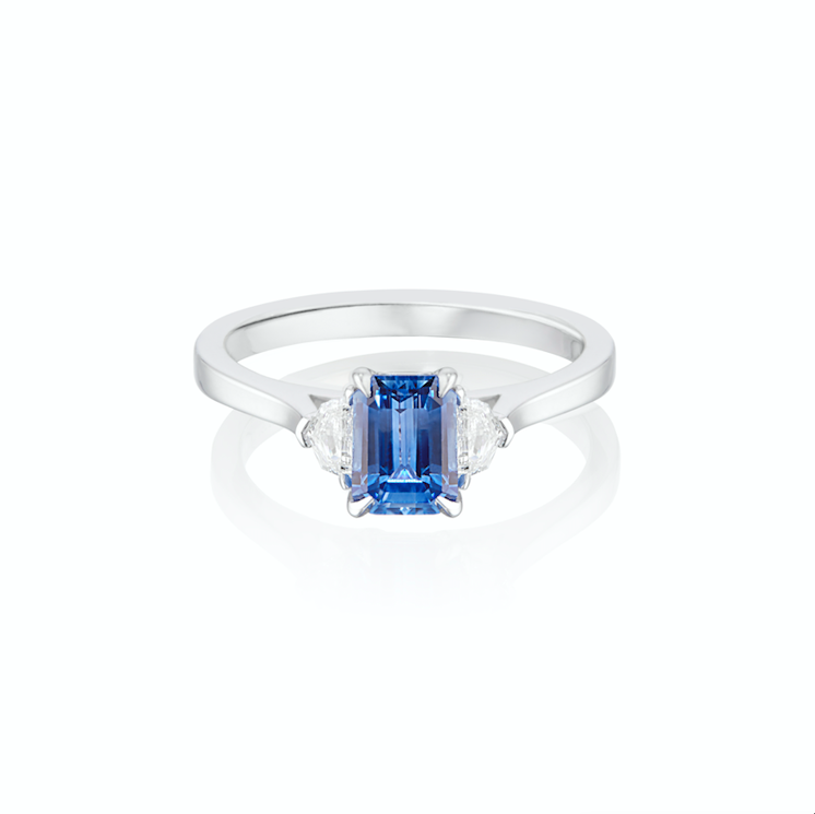 White gold ring with a central blue sapphire gemstone flanked by two smaller white diamonds.