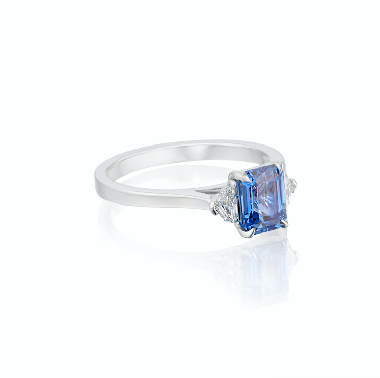 White gold ring with blue sapphire gemstone flanked by two small diamonds, isolated on a white background.