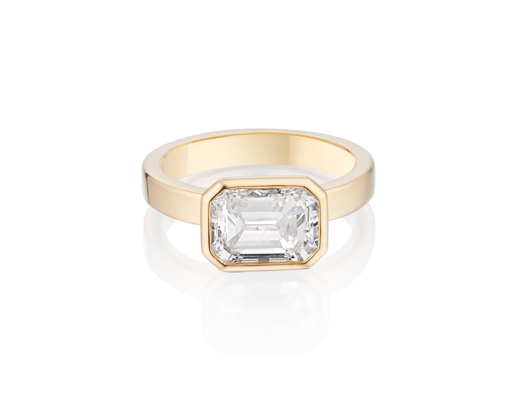 Gold ring with a single Emerald Cut diamond, on a white background.