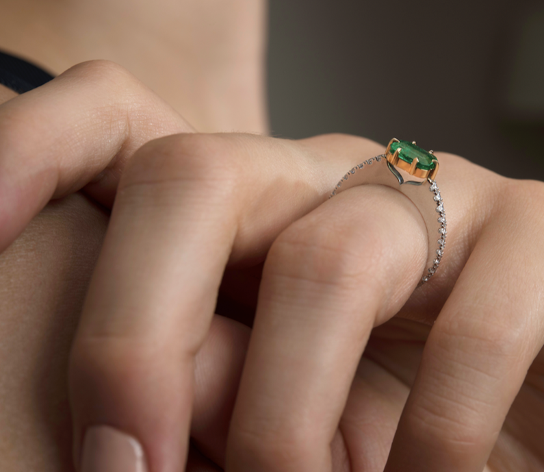 Close-up of a hand wearing a ring with a green gemstone and diamond accents.