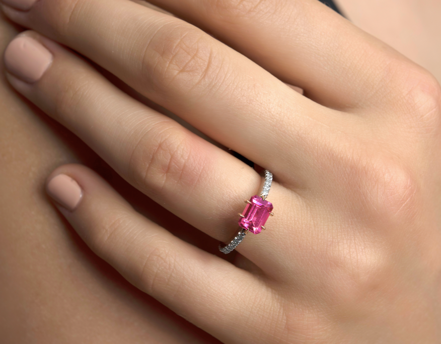 A hand wearing a ring with a large pink gemstone surrounded by small diamonds.