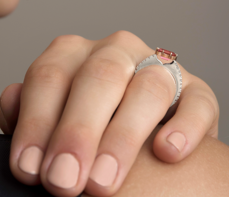 Hand wearing a ring with a pink gemstone.