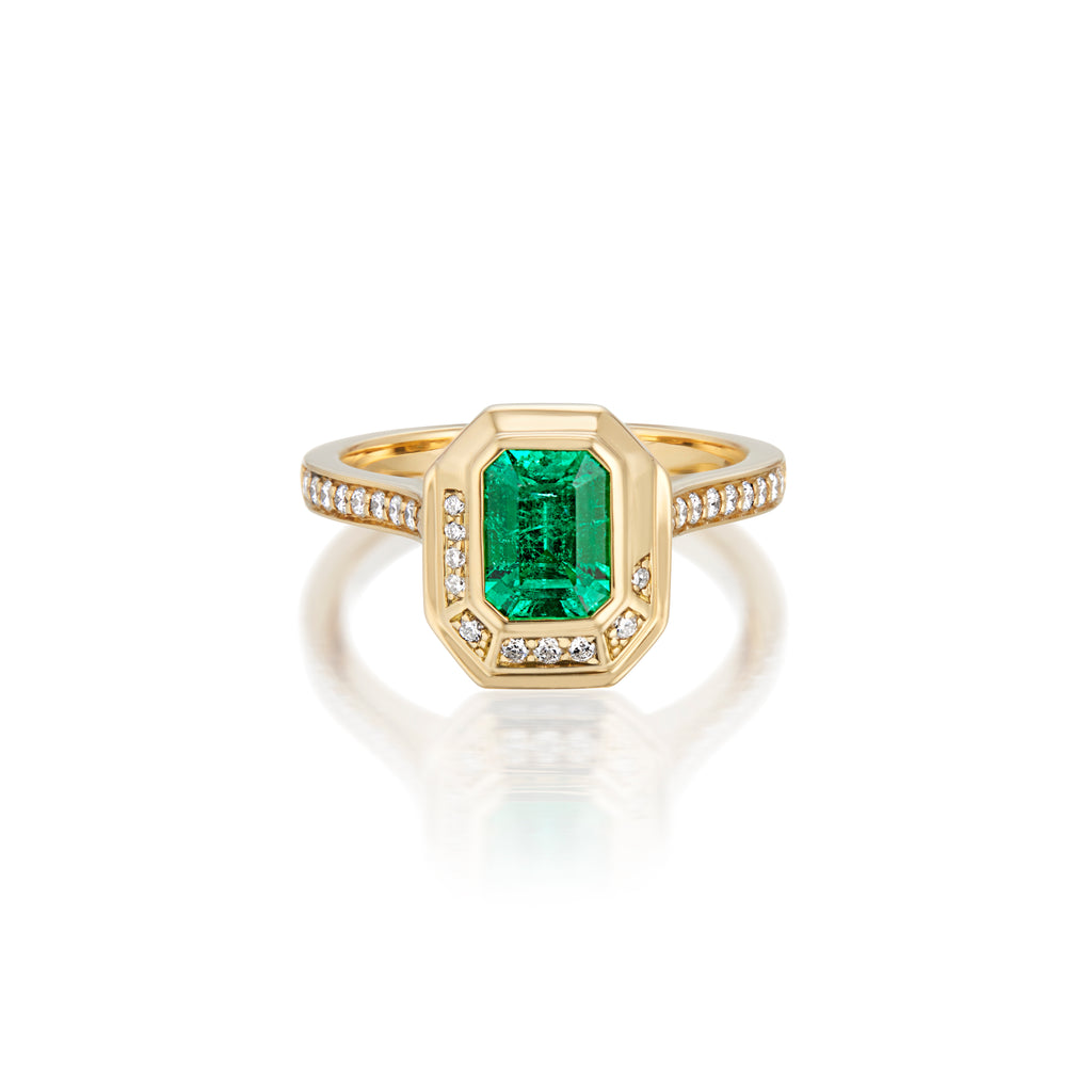 Gold ring with rectangular emerald and diamond accents on a reflective surface.