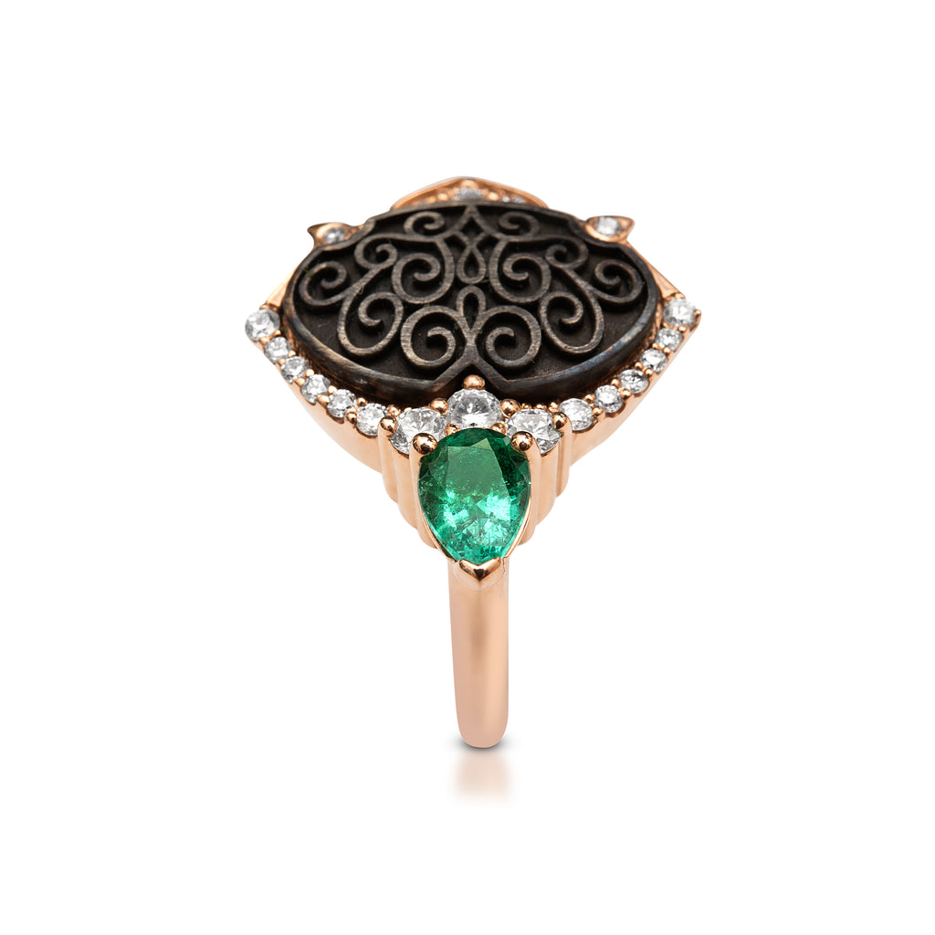 An ornate rose gold ring with a central green emerald and diamond halo on a black background.