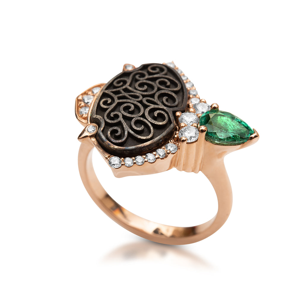 Gold ring with black filigree engraving, diamonds, and a green emerald against a white background.