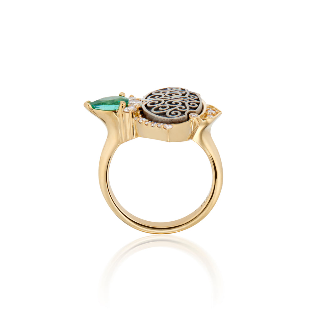 Gold ring with an intricate black and gold patterned top, accented with a green gemstone and diamonds.