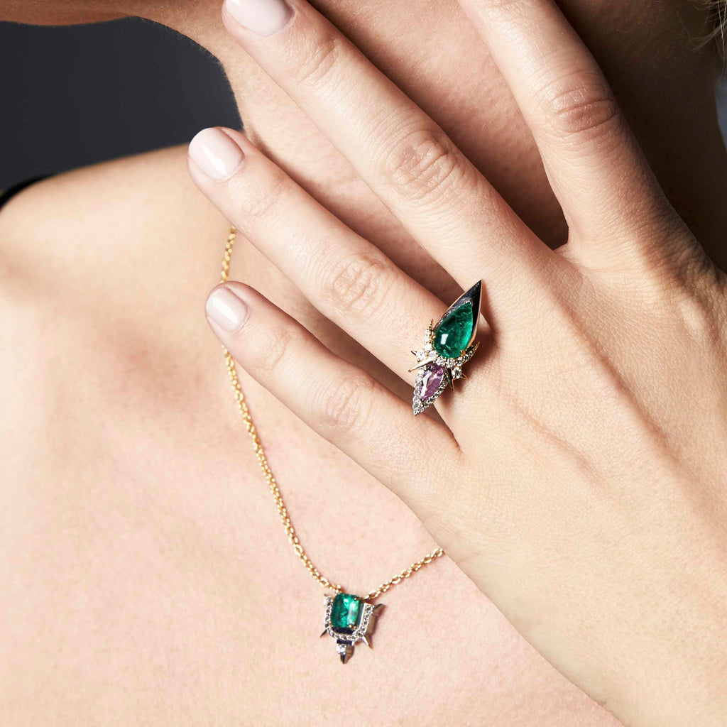 A hand displaying a jeweled ring and a matching pendant necklace on a gold chain.