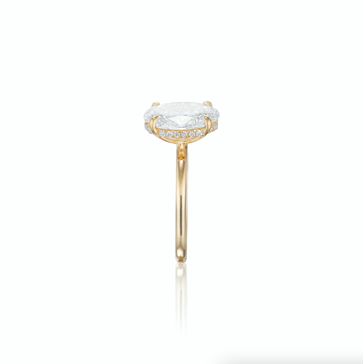 Gold ring with a large oval diamond and small surrounding diamonds, on a white background.