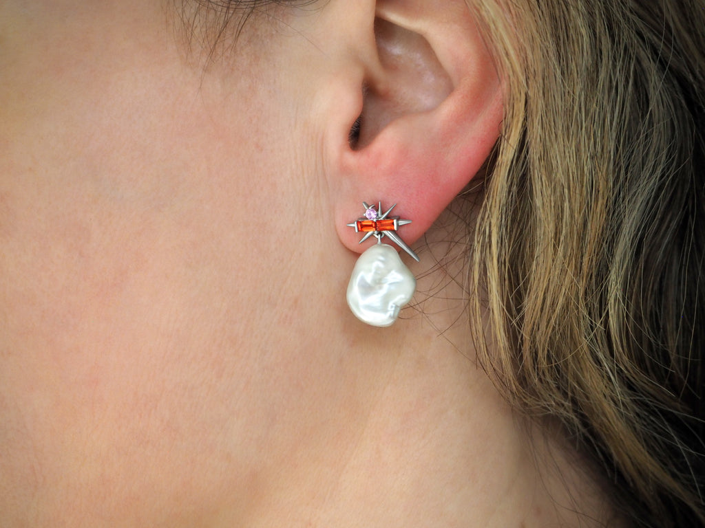 A close-up of a woman's ear with a unique bar-shaped earring with a pearl drop.