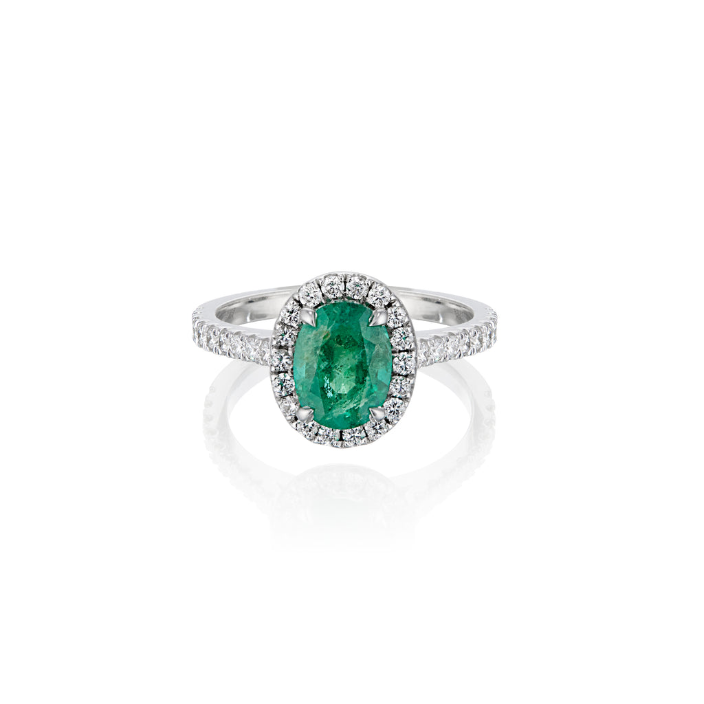 Oval emerald ring with diamond halo and band on a white background.