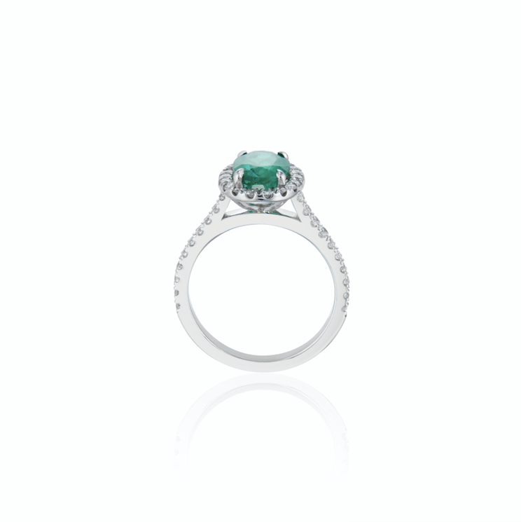 White gold ring with a central emerald flanked by small diamonds on a reflective white surface.