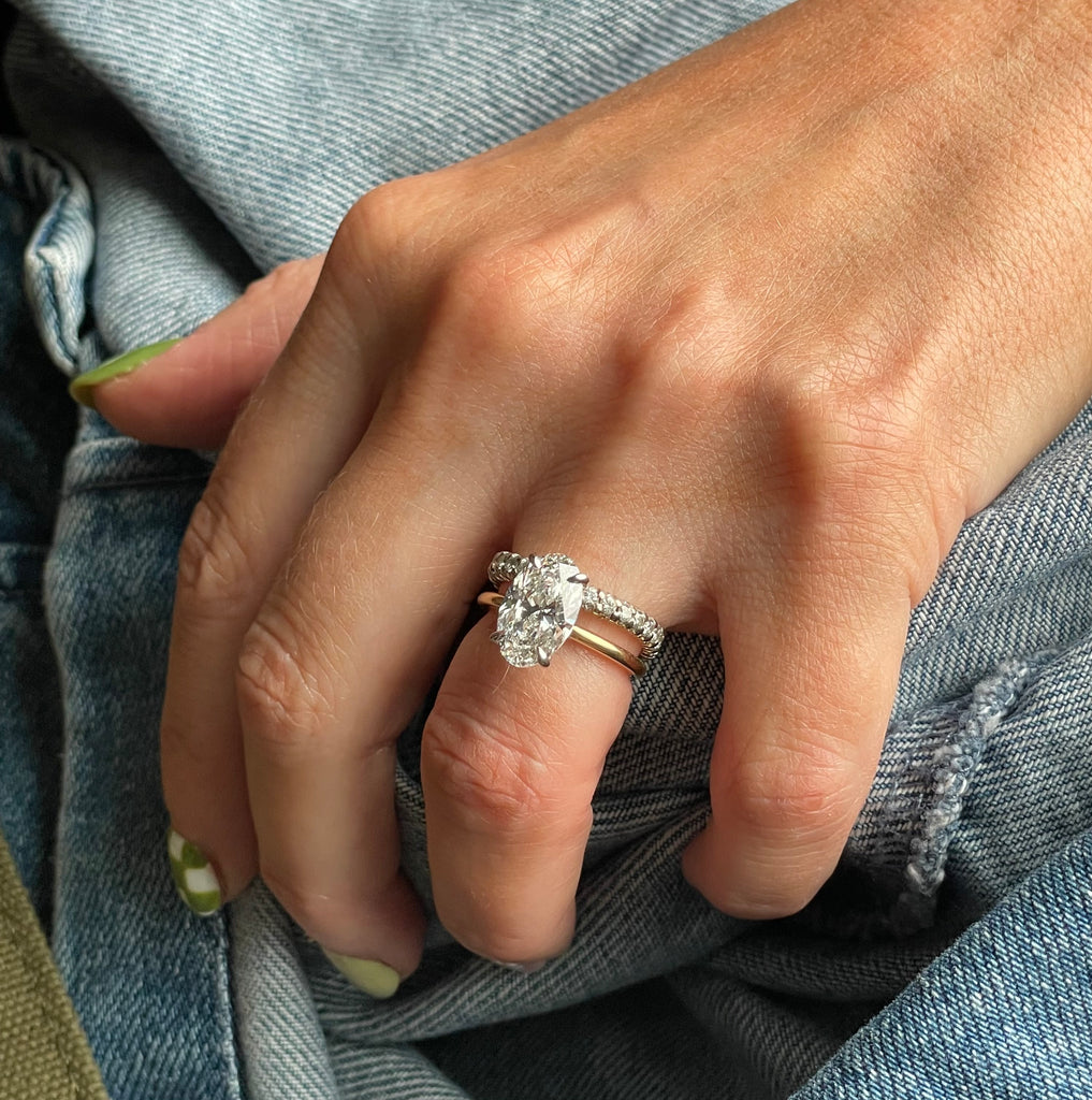 A hand with a diamond ring on the ring finger, resting on blue denim fabric.