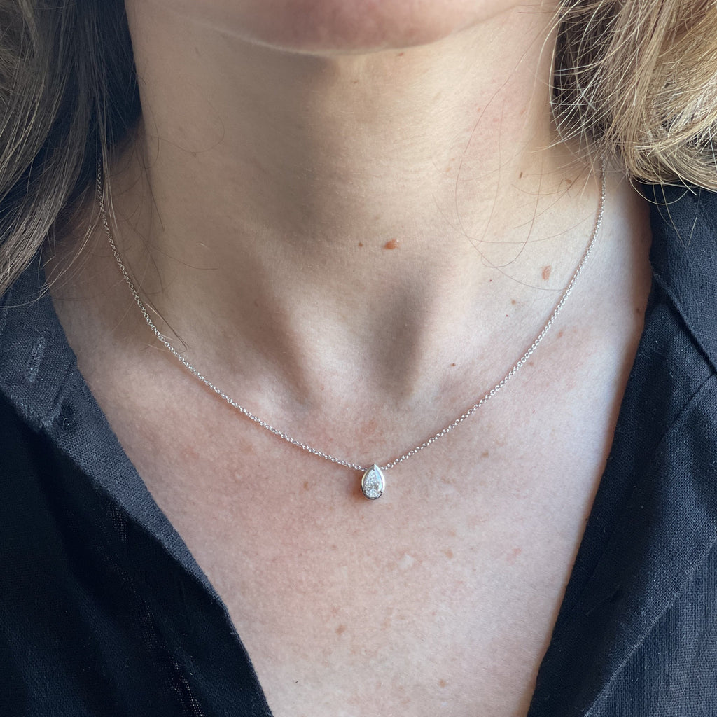 Woman wearing a pear-shaped single solitaire diamond necklace on a white chain