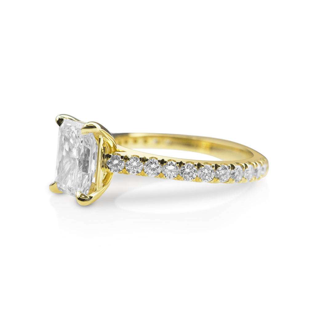 A gold engagement ring with a central radiant-cut diamond and smaller round diamonds on the band.