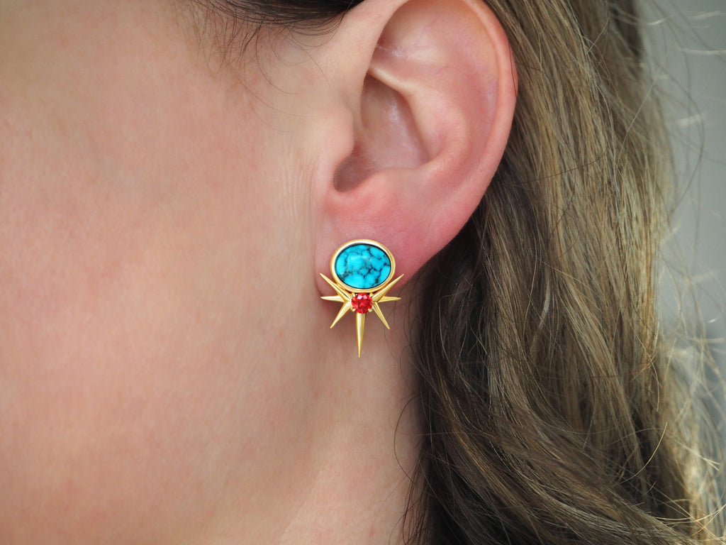 A person's ear with a turquoise and gold sunburst earring.