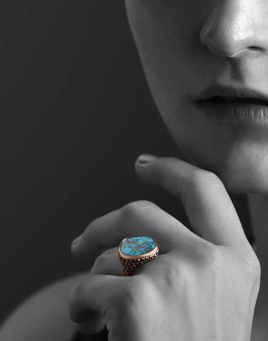 Hand with turquoise ring against a dark background.