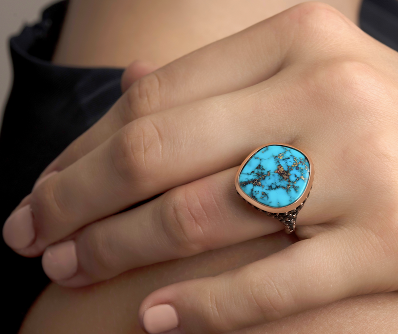 Close-up of a hand wearing a turquoise ring with a copper matrix on a finger.