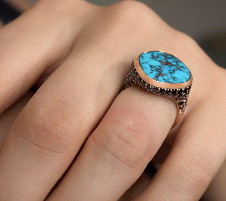 A turquoise ring with a detailed small black diamond band on a finger.