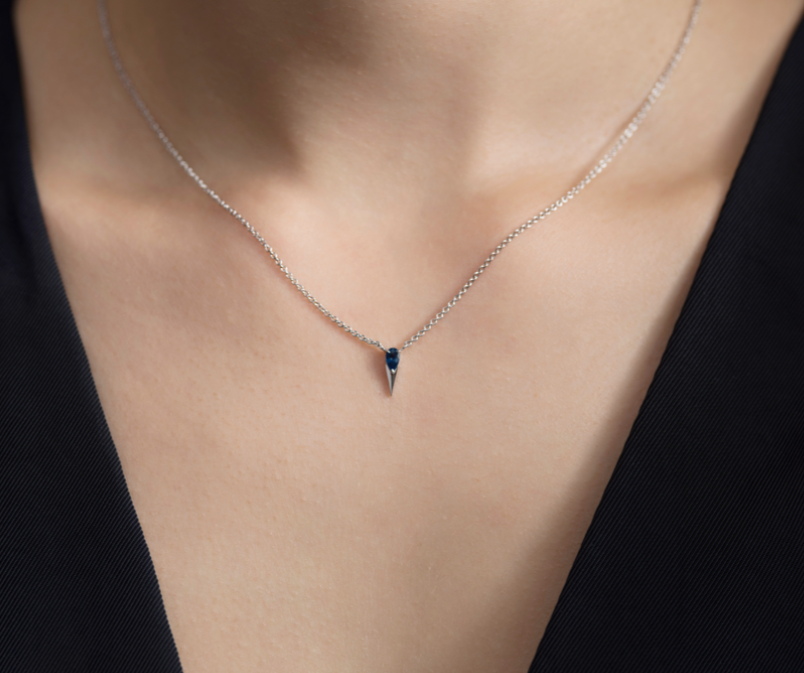 Close-up of a person wearing a black garment with a visible neckline featuring a blue sapphire.