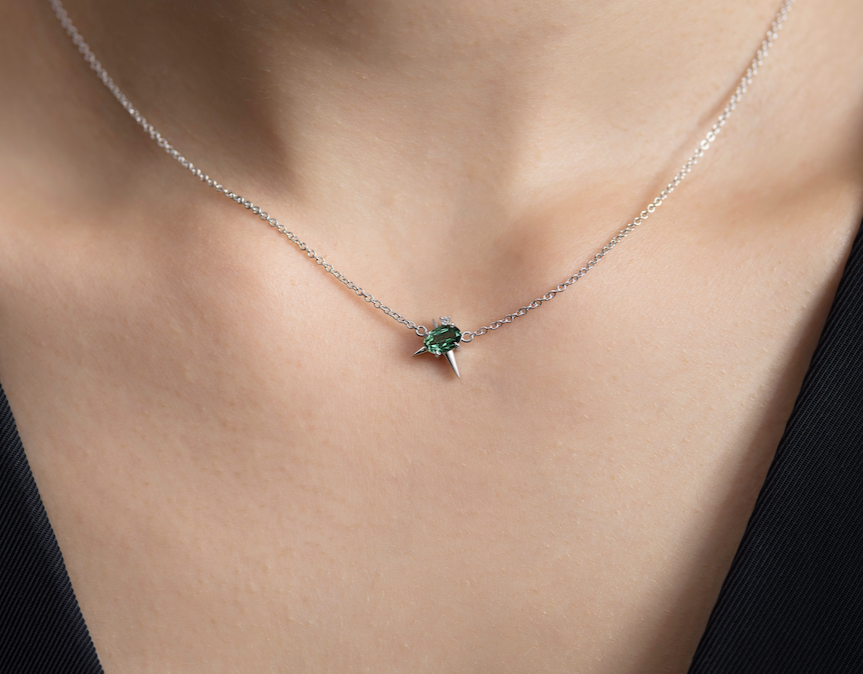 Close-up of a person's neck wearing a white gold chain necklace with a green tourmaline and diamond.