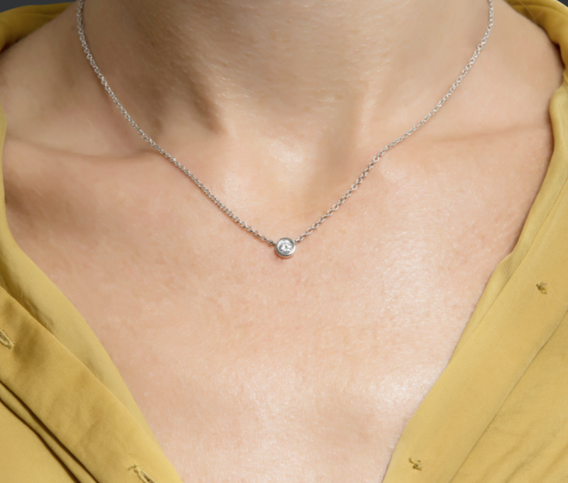 Close-up of a white gold necklace with a single diamond pendant on a person's neck.