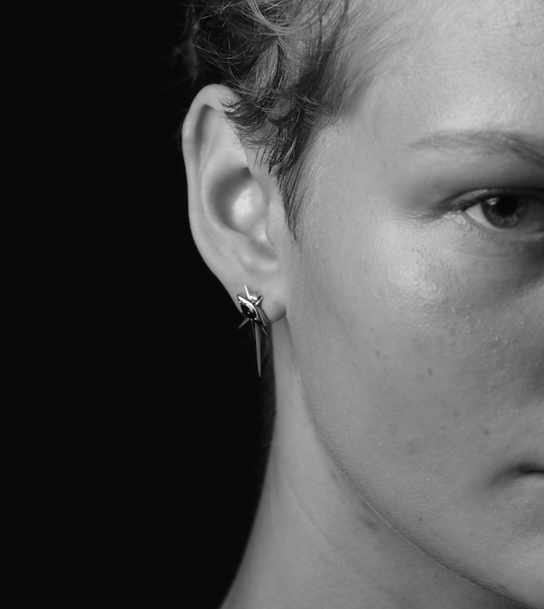 Close-up of an ear with a star-shaped earring against a black background.