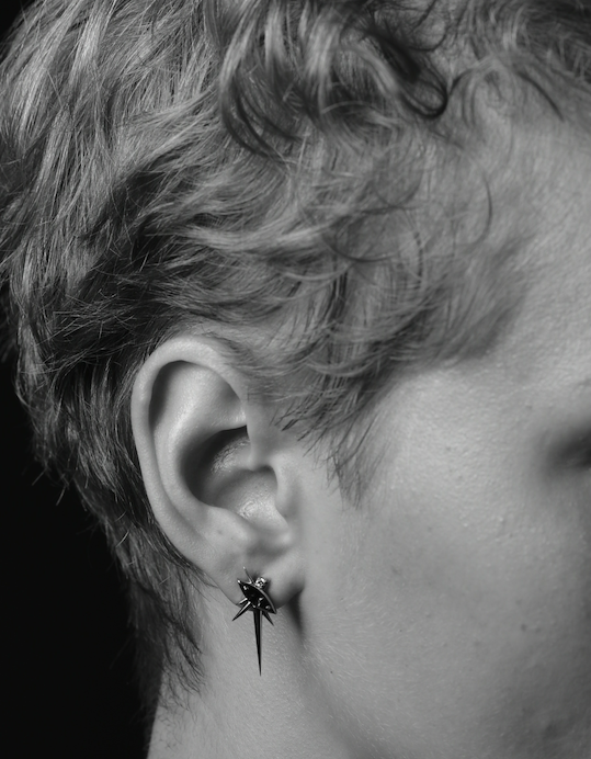 Close-up of an ear with a spider-shaped earring, in black and white.